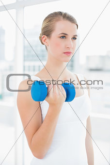 Pensive fit woman exercising with dumbbells