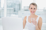 Pretty blonde holding glass of water using her laptop