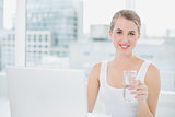 Cute blonde holding glass of water using her laptop