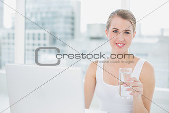 Cute blonde holding glass of water using her laptop