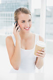 Cheerful blond woman on the phone holding coffee