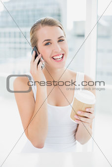 Smiling blond woman on the phone holding coffee
