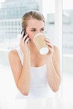 Smiling blond woman on the phone drinking coffee