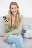 Cheerful pretty blonde text messaging while sitting on cosy sofa