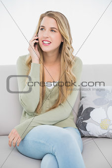 Cheerful pretty blonde on the phone sitting on cosy sofa