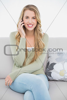 Happy pretty blonde on the phone sitting on cosy sofa