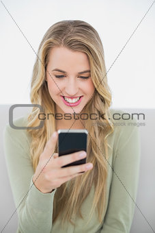 Smiling pretty blonde sending a text sitting on cosy sofa