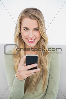 Cheerful pretty blonde sending a text sitting on cosy sofa