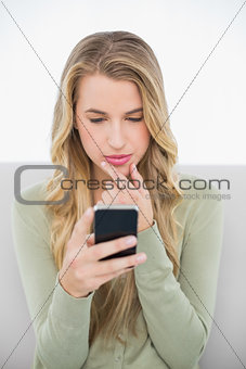 Thinking pretty blonde sending a text sitting on cosy sofa