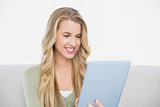 Smiling pretty blonde using her tablet sitting on cosy sofa