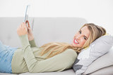 Cheerful pretty blonde using her tablet lying on cosy sofa