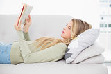 Pretty blonde reading book lying on cosy sofa