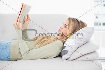 Pretty blonde reading book lying on cosy sofa