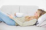 Pretty blonde holding popcorn lying on cosy sofa