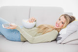 Smiling pretty blonde holding popcorn lying on cosy sofa