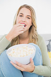 Happy pretty blonde eating popcorn sitting on cosy sofa