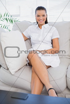 Smiling woman in white dress sitting on sofa