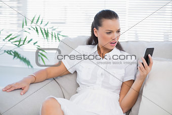 Irritated woman in white dress looking at her smartphone