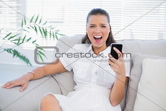 Angry woman holding her phone screaming at camera
