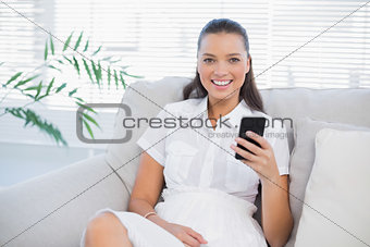 Smiling woman sitting on sofa using her phone