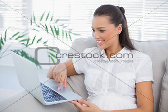 Cheerful pretty woman using laptop sitting on cosy sofa