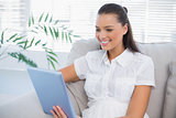 Happy cute woman using tablet sitting on cosy sofa
