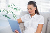Serious cute woman using tablet sitting on cosy sofa