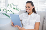 Smiling cute woman using tablet sitting on cosy sofa