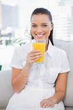Smiling pretty woman holding orange juice sitting on cosy couch