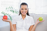 Smiling woman holding red and green apple sitting on sofa