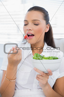 Peaceful pretty woman eating healthy salad sitting on sofa
