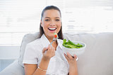 Smiling pretty woman holding healthy salad sitting on sofa