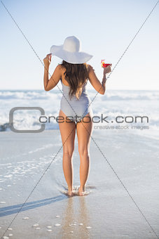Rear view of woman in swimsuit with straw hat holding cocktail