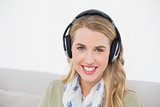 Smiling cute blonde listening to music sitting on cosy sofa