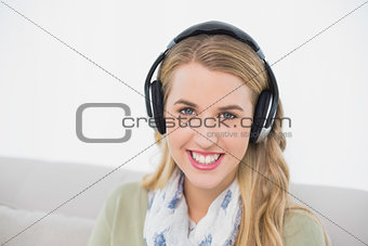 Smiling cute blonde listening to music sitting on cosy sofa