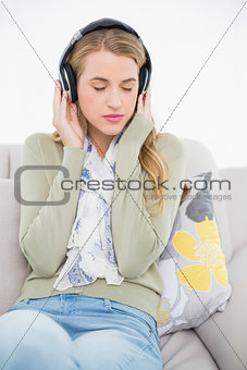 Relaxed cute blonde listening to music sitting on cosy sofa