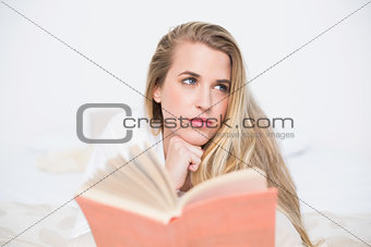 Pensive gorgeous model lying on cosy bed holding book