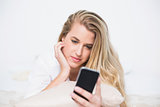Content gorgeous model looking at her smartphone lying on cosy bed