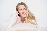 Smiling model on the phone lying on cosy bed