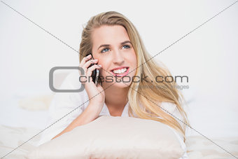 Smiling model on the phone lying on cosy bed