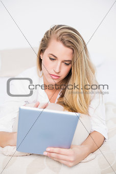 Focused model using her tablet lying on cosy bed