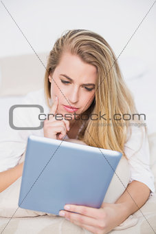 Concentrated model using her tablet lying on cosy bed