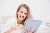 Smiling pretty model using her tablet pc lying on cosy bed