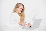 Smiling pretty model using her laptop lying on cosy bed