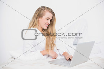 Smiling pretty model using her laptop lying on cosy bed