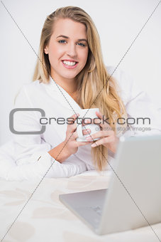 Happy pretty model holding coffee lying on cosy bed