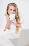 Smiling pretty model drinking coffee lying on cosy bed