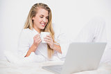 Smiling cute model holding coffee lying on cosy bed