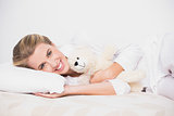 Cheerful cute model lying on cosy bed with teddy bear