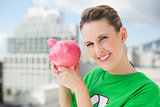 Smiling woman wearing green recycling tshirt holding piggy bank